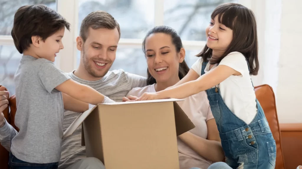 Una familia sentada en un sofá, rodeada de un ambiente acogedor, con una caja en el centro.